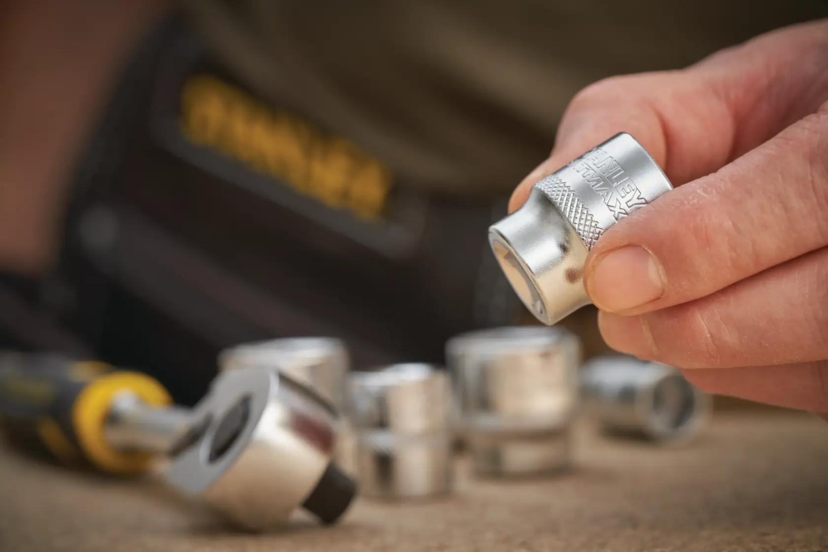 STANLEY FMMT17210-0 socket set photography, close-up of hand holding socket with ratchet and other sockets nearby.