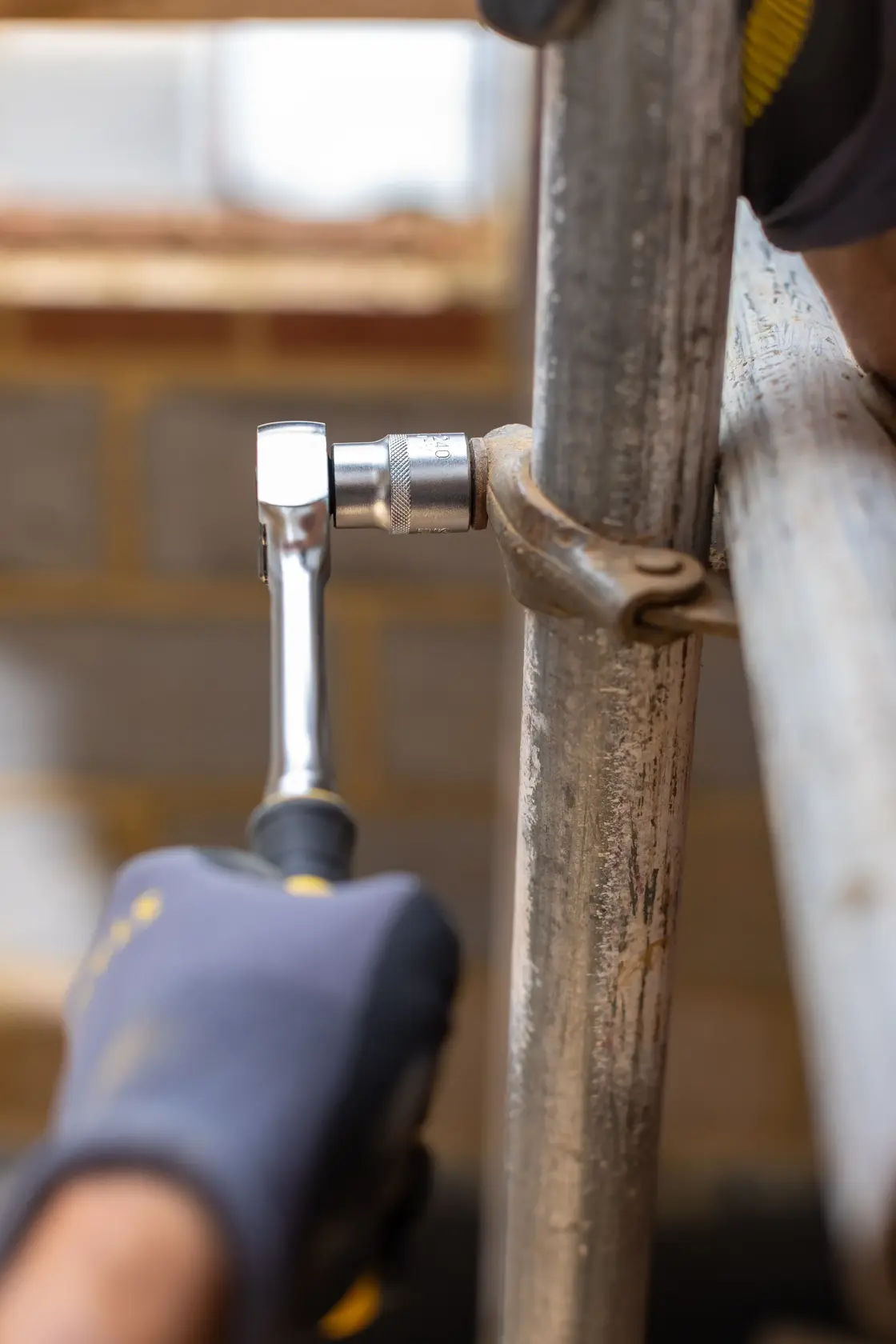 STANLEY FMMT17210-0 ratchet wrench used to tighten clamp on metal pipe, side view, in construction setting.