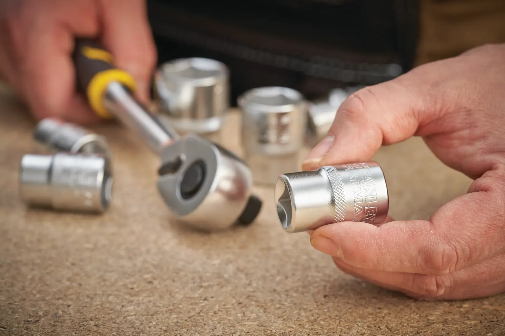 STANLEY FMMT17240-0 photography of hand holding socket wrench with metal sockets on tabletop.