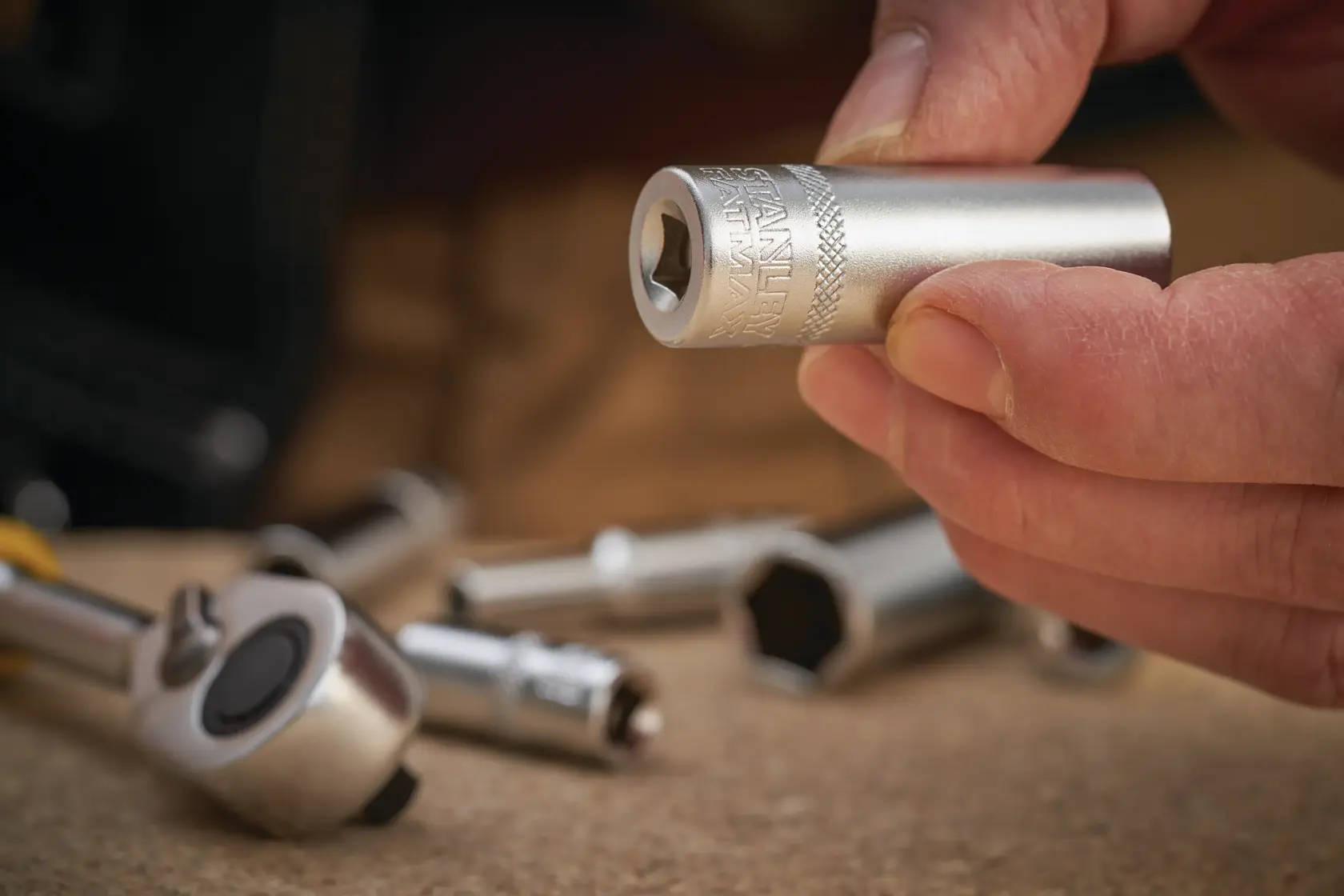 Photo of STANLEY FMMT17339-0 socket held in hand, silver finish, with ratchet tool and other sockets blurred in background.