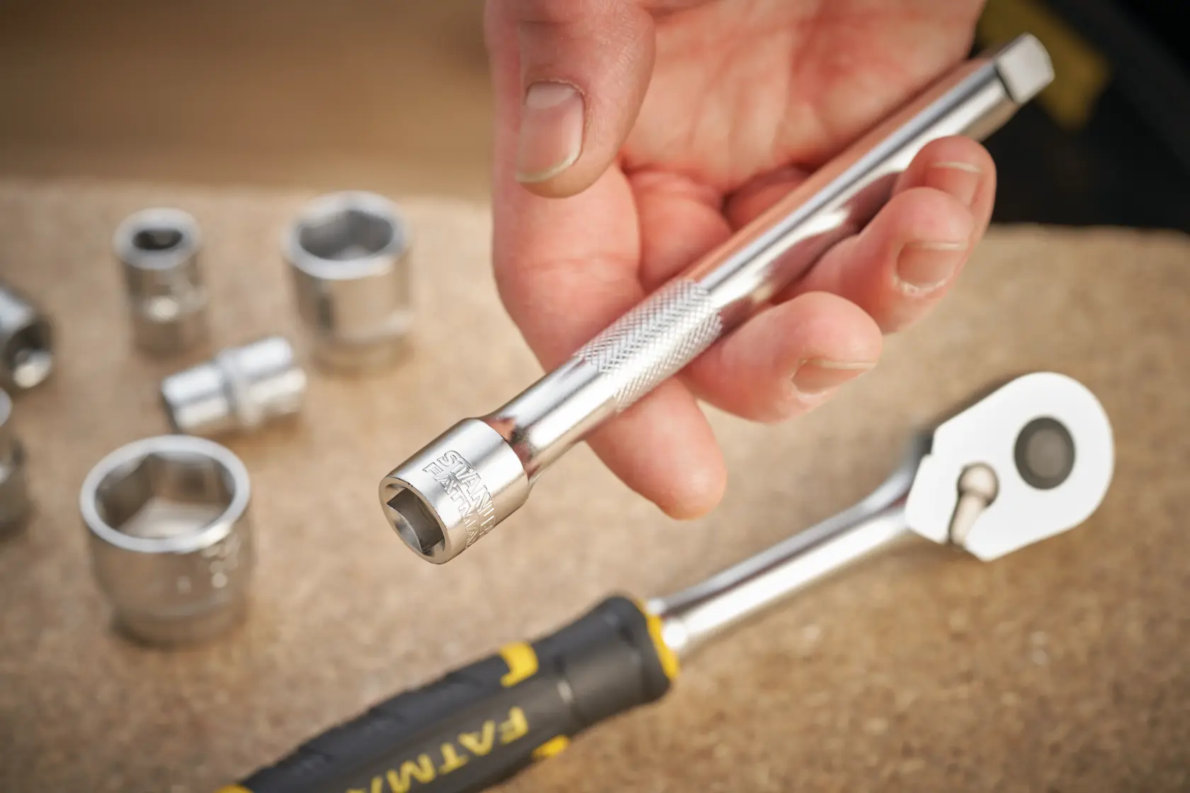 STANLEY FMMT25131-0 socket extension bar held by hand, with chrome sockets and ratchet on workbench.
