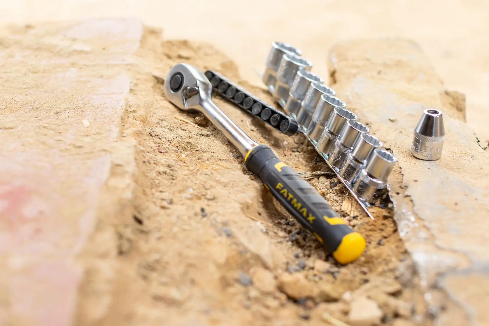 STANLEY FMMT82680-0 ratchet and socket set with yellow and black handle on sandy ground, front angle.