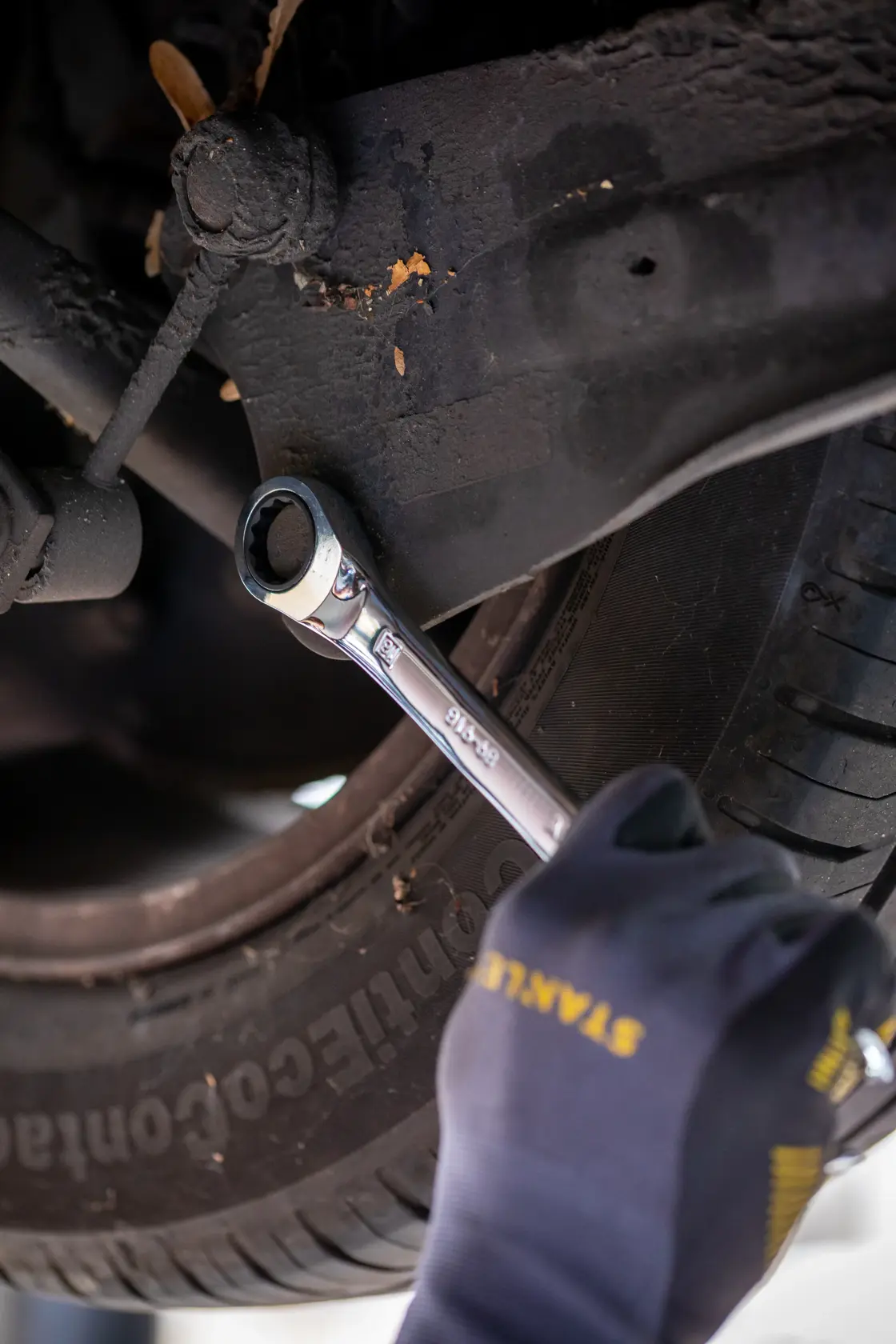 Photo of STANLEY FMMT82849-0 ratcheting wrench in use on car suspension bolt, mechanic wearing STANLEY gloves.