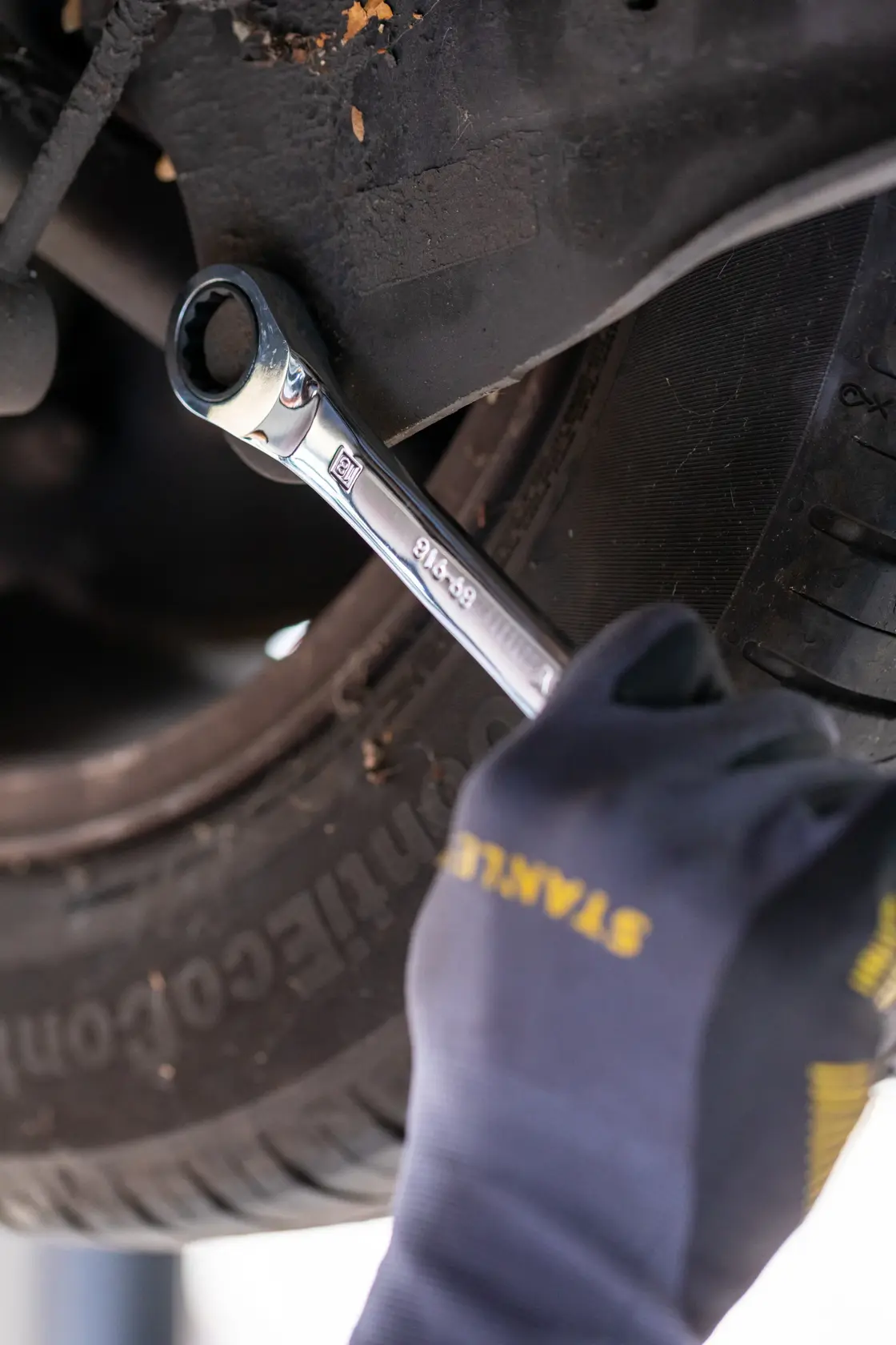 Photo of STANLEY FMMT82849-0 ratcheting wrench in use on a car, hand wearing STANLEY glove.