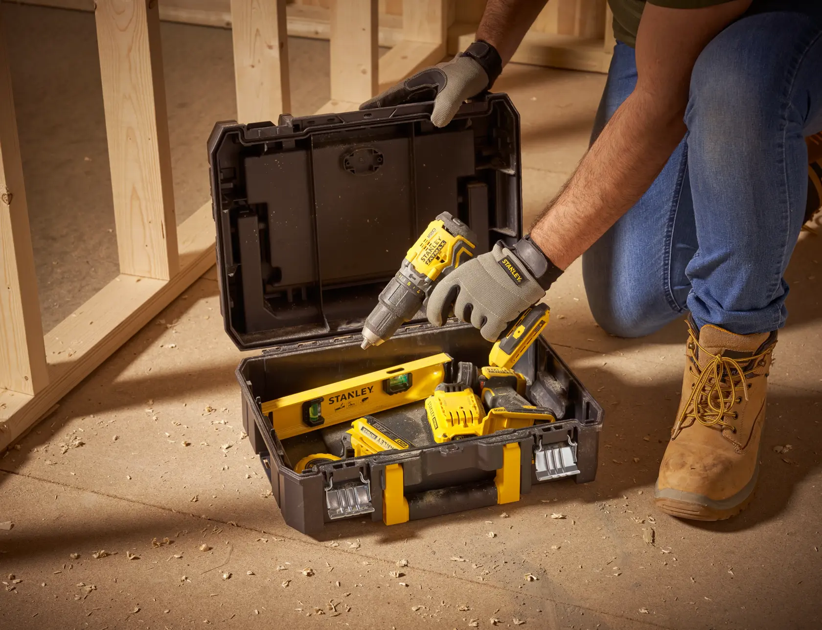 STANLEY FMST1-71967 toolbox with yellow and black hand tools on construction site floor, lid open.