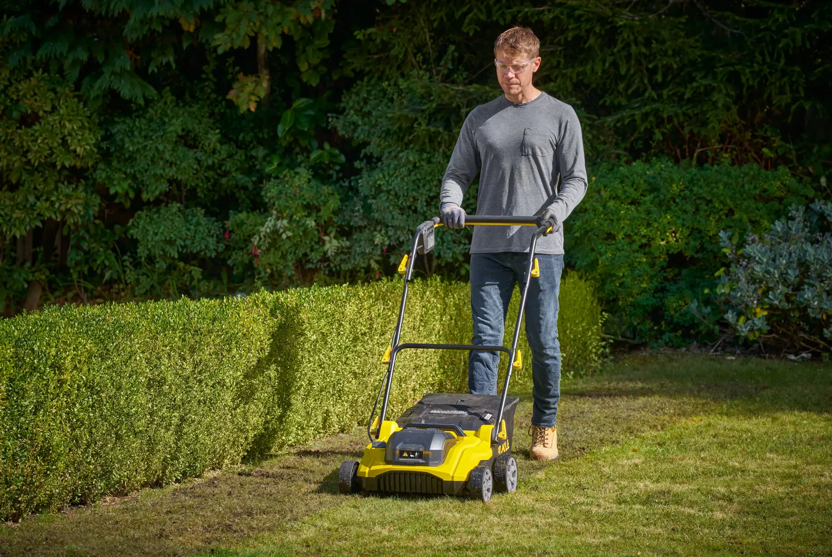 Photo of STANLEY SCOEP3801M2 lawn scarifier in use on a garden lawn, operated by a person outdoors.