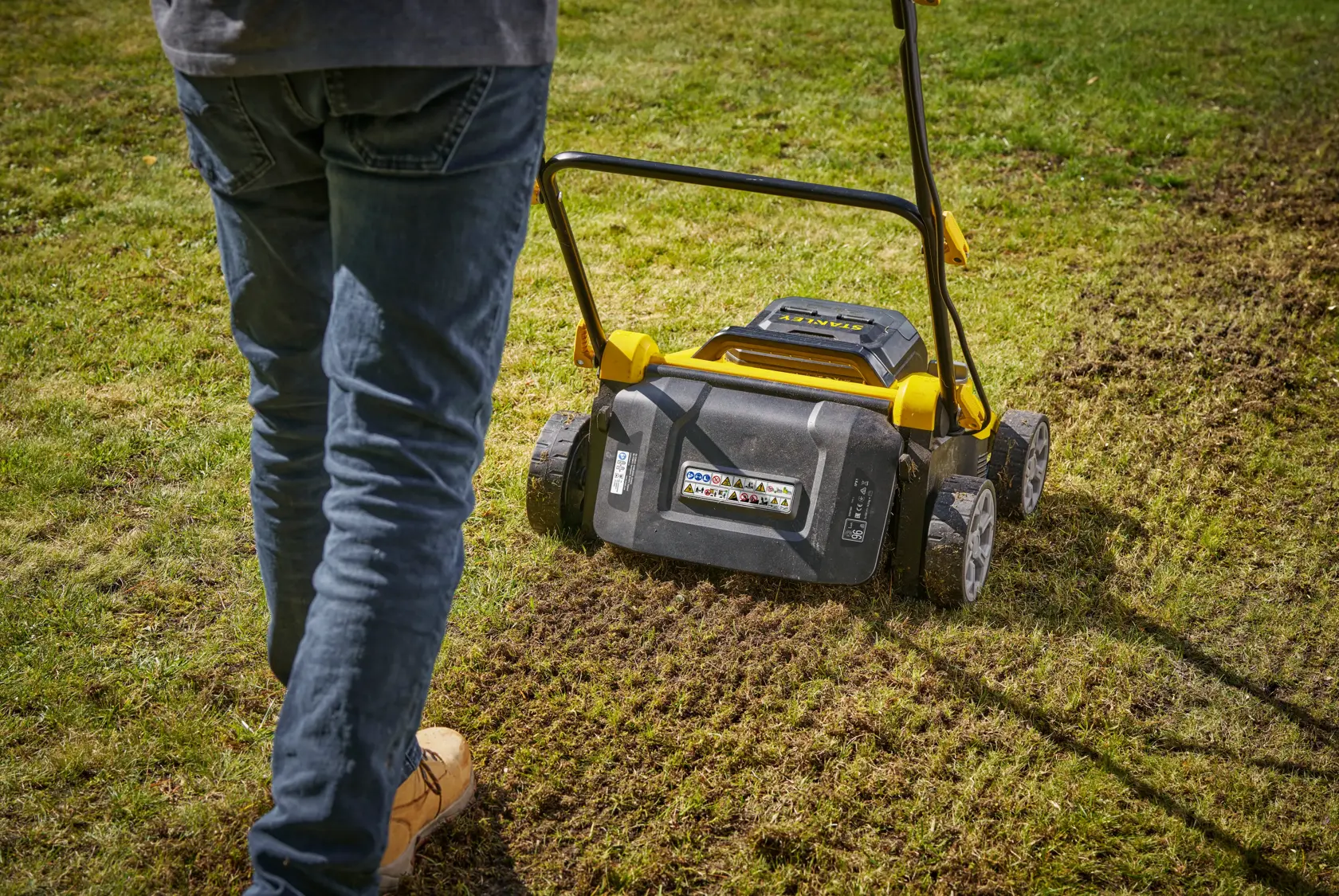 STANLEY SCOEP3801M2 lawn scarifier in use on grass, rear view showing wheels and handle.