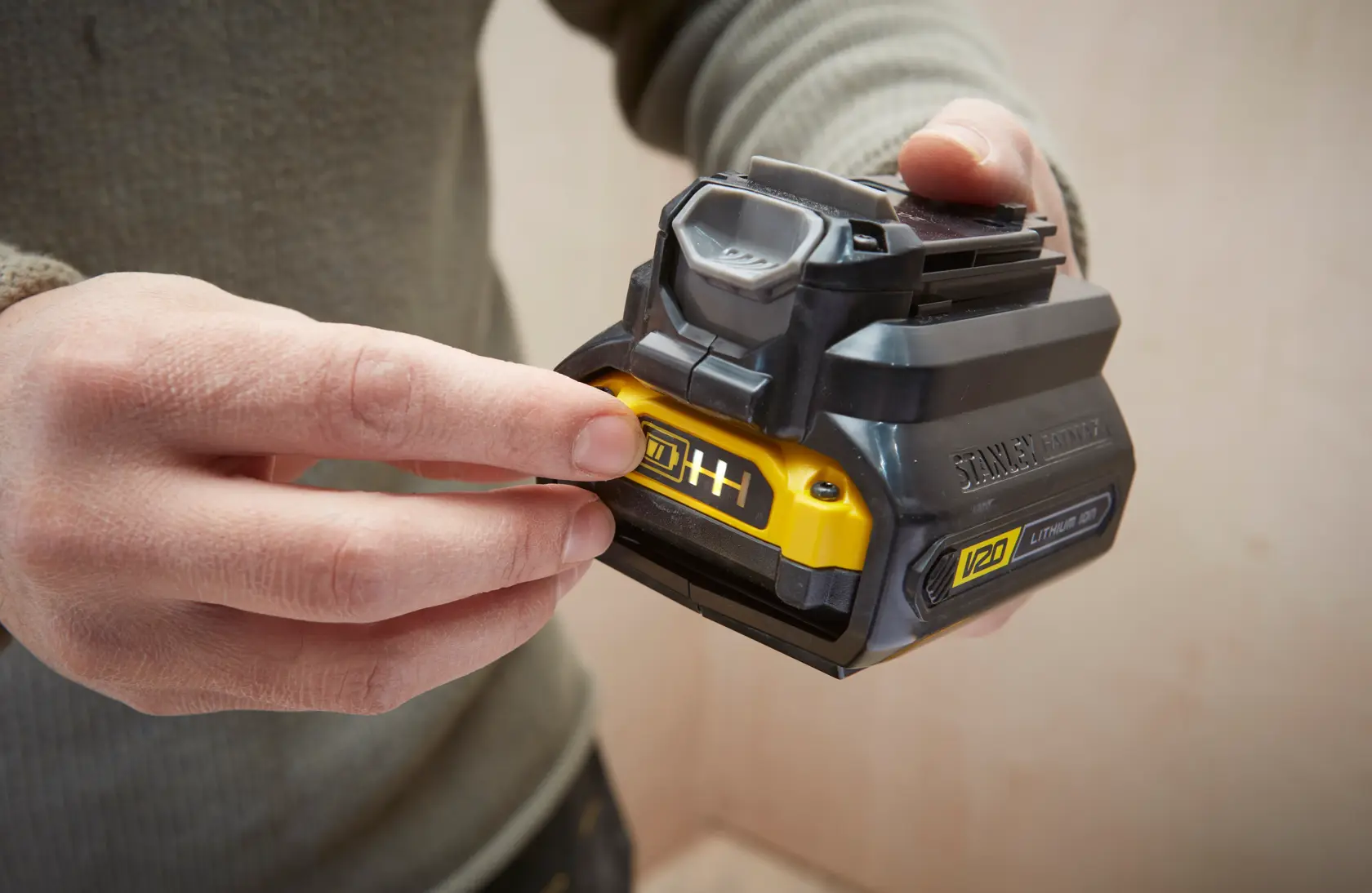 Photo of a hand holding a STANLEY V20 lithium-ion battery, SKU SFMCB100, with charge indicator, close-up view.