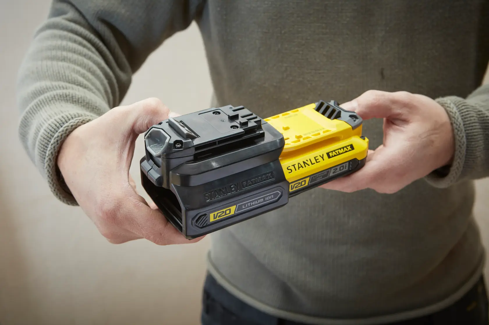 Photo of hands holding STANLEY FATMAX SFMCB100 V20 lithium-ion batteries, one black and one yellow.