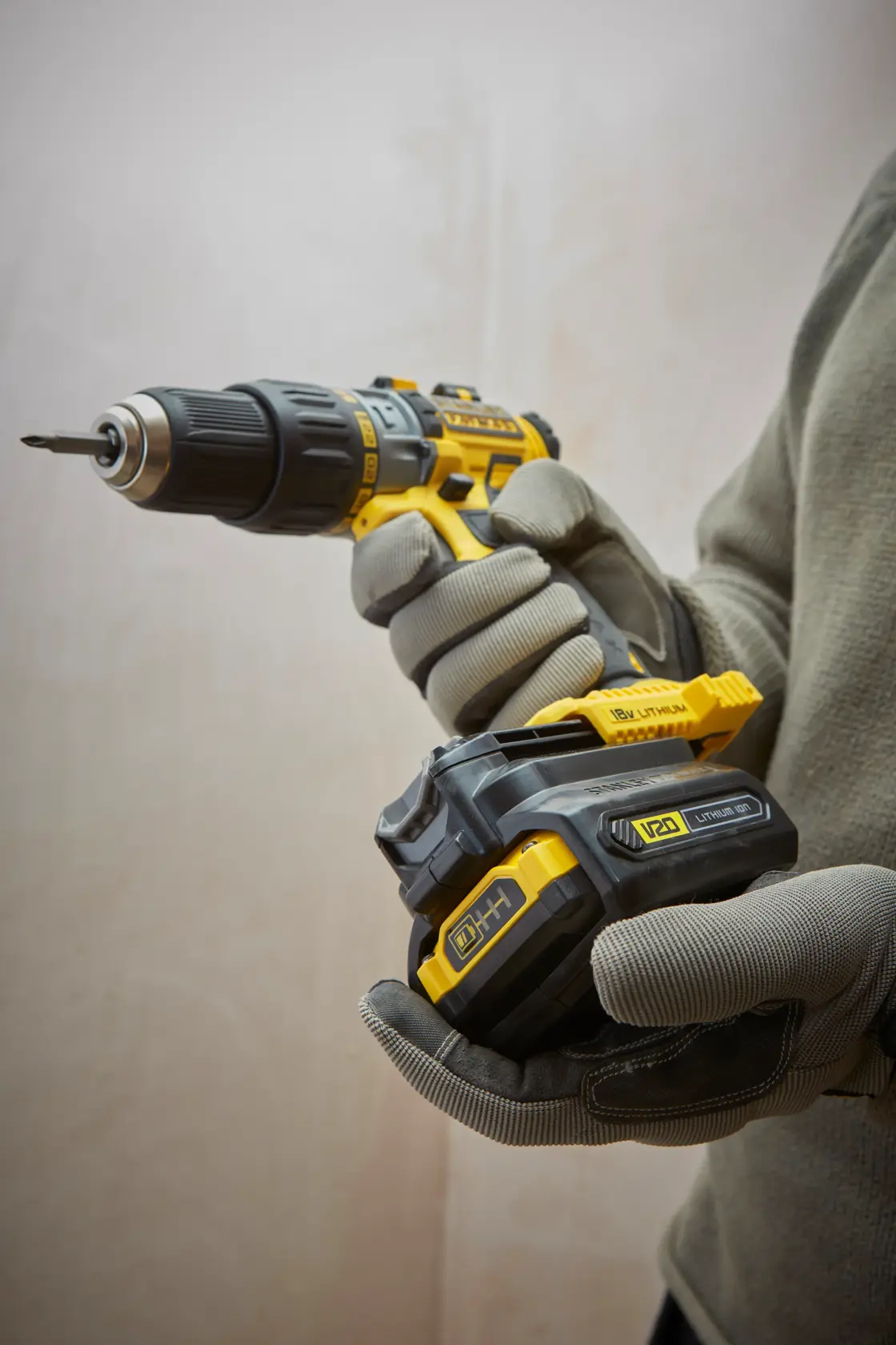 STANLEY SFMCB100 cordless drill with V20 lithium battery, close-up view in use, grey gloves visible.