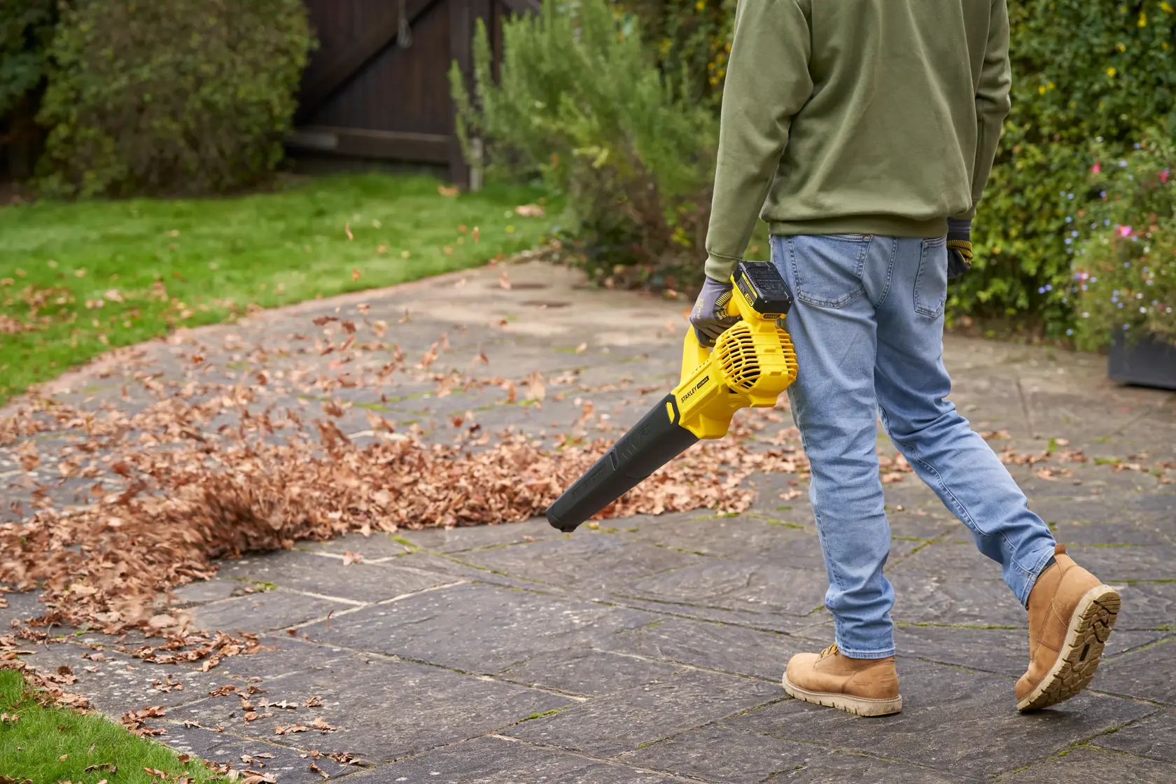 Photo of a person using a STANLEY SFMCBL714B-XJ cordless leaf blower on a patio covered with autumn leaves.