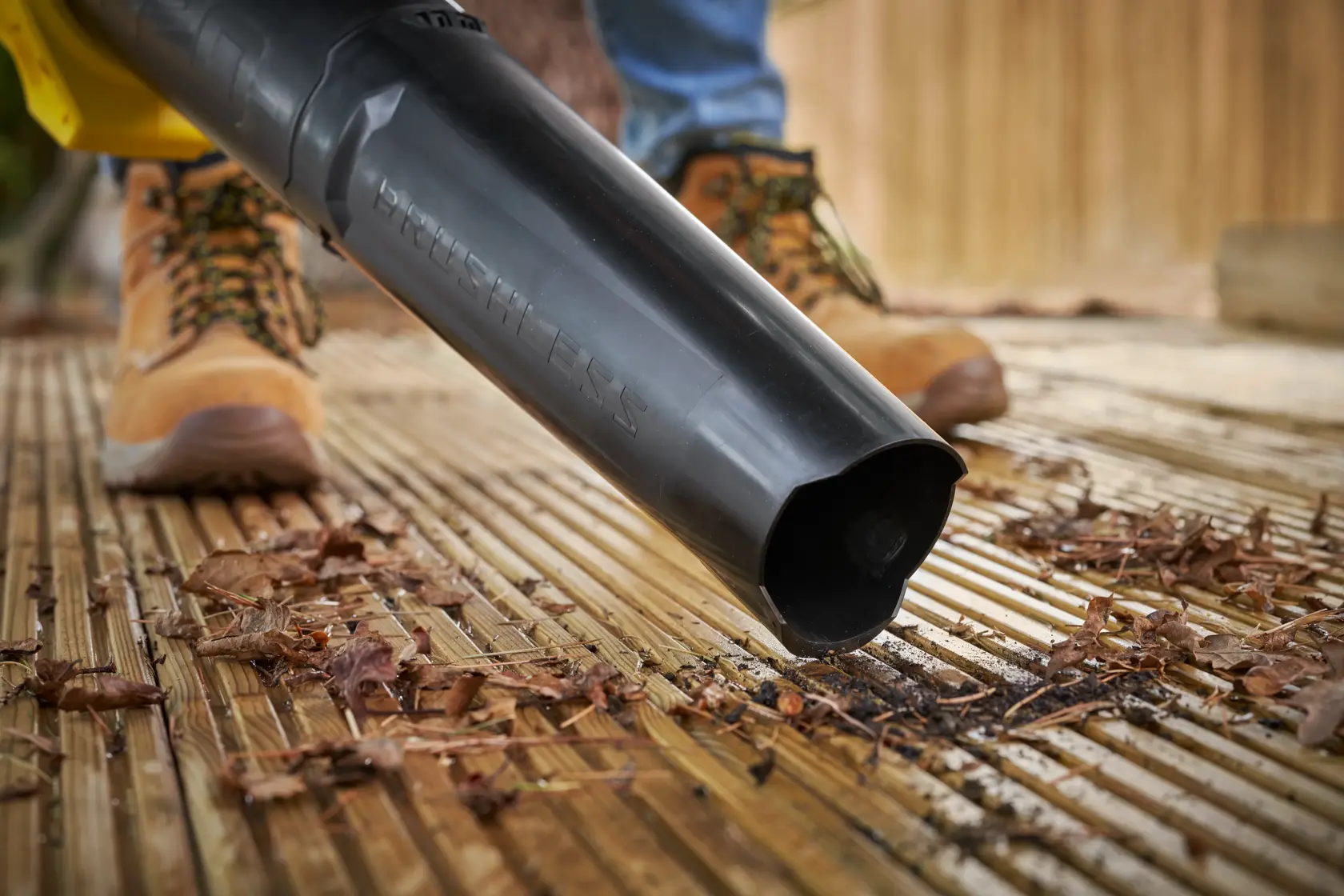 STANLEY SFMCBL730M1 leaf blower in action on wooden deck, close-up of nozzle clearing leaves.
