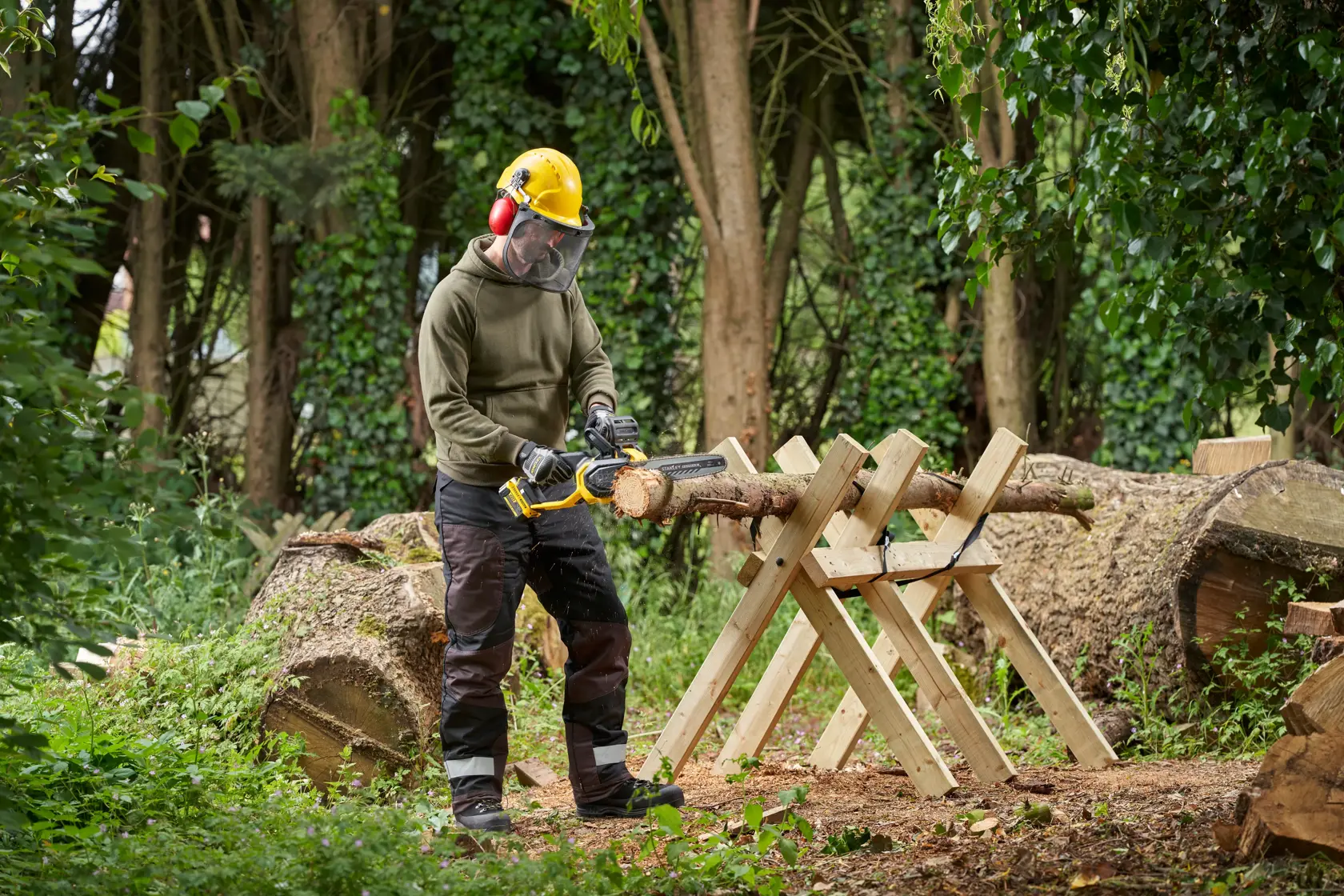 Photo of person using STANLEY SFMCCS730B chainsaw to cut wood on a sawhorse outdoors.