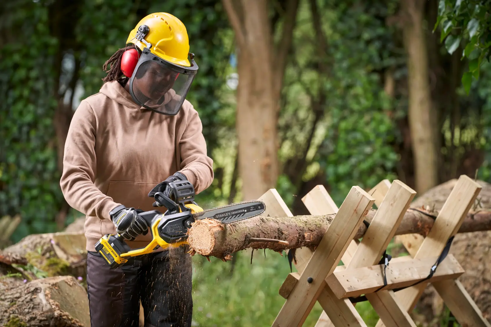Photo of STANLEY SFMCCS730B chainsaw in use cutting a log outdoors, with operator wearing safety gear.