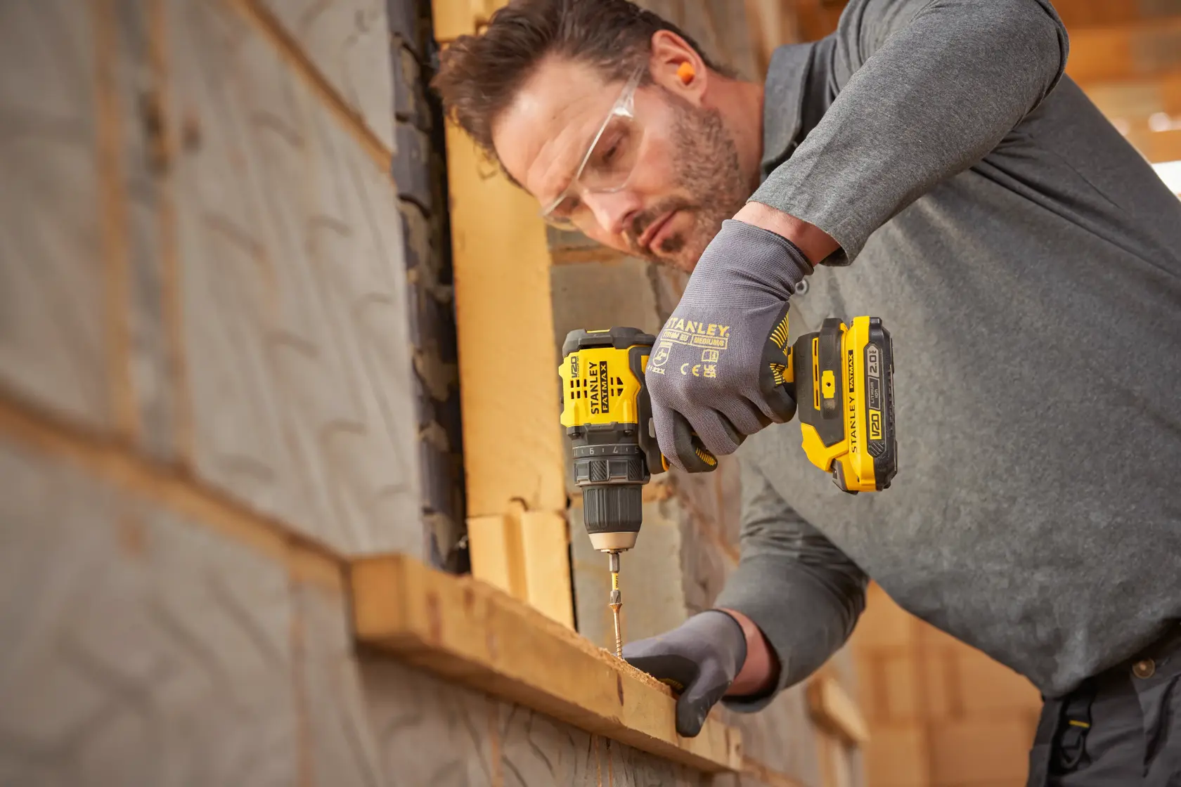 Photo of a person using a STANLEY SFMCD714B-XJ cordless drill, driving a screw into wood at a construction site.