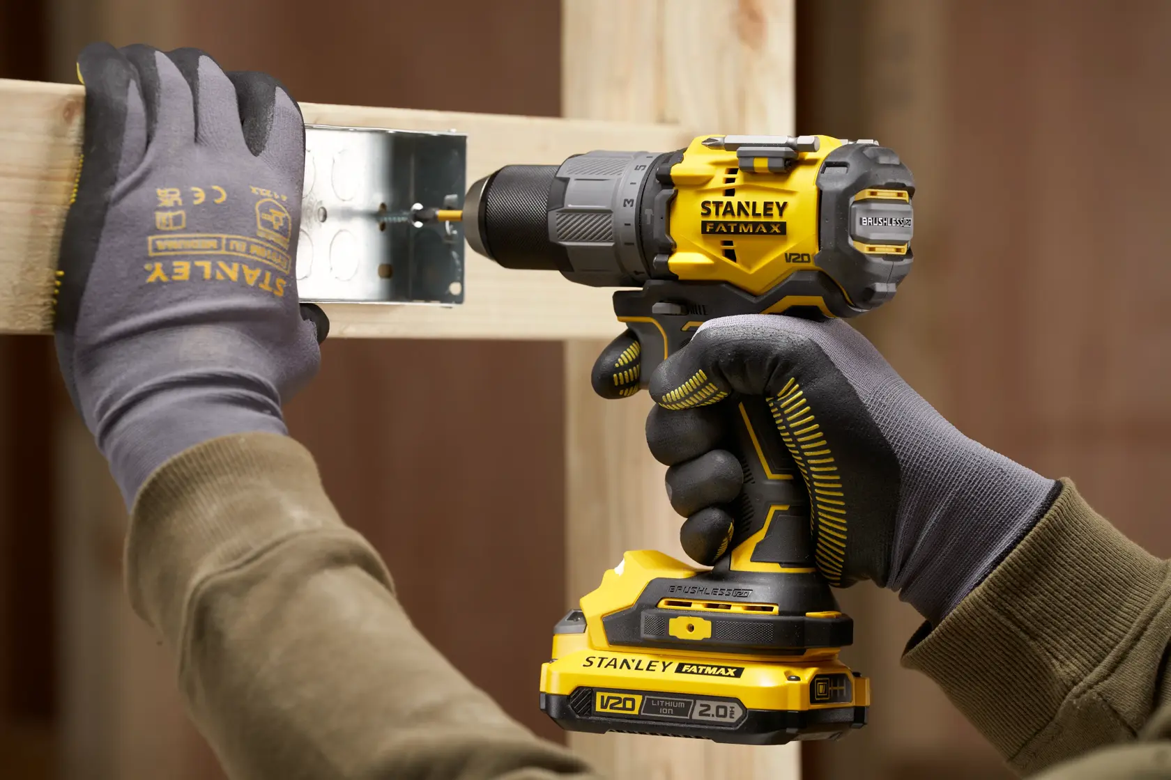 Photo of STANLEY SFMCD726D2K cordless drill in use on wooden beam, close-up of hands with gloves.