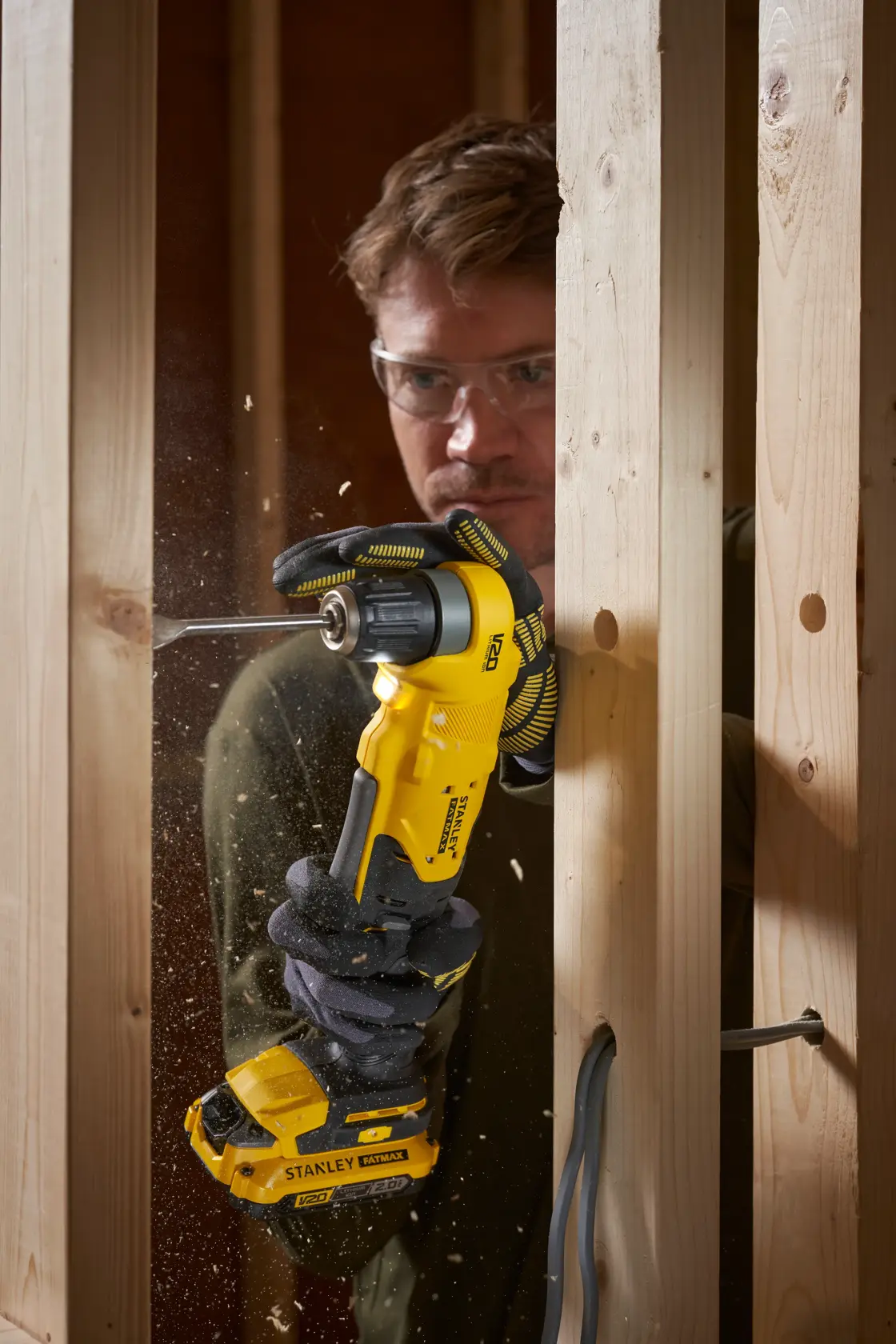 STANLEY SFMCD750B cordless angle drill in use drilling through wood studs, close-up action shot.