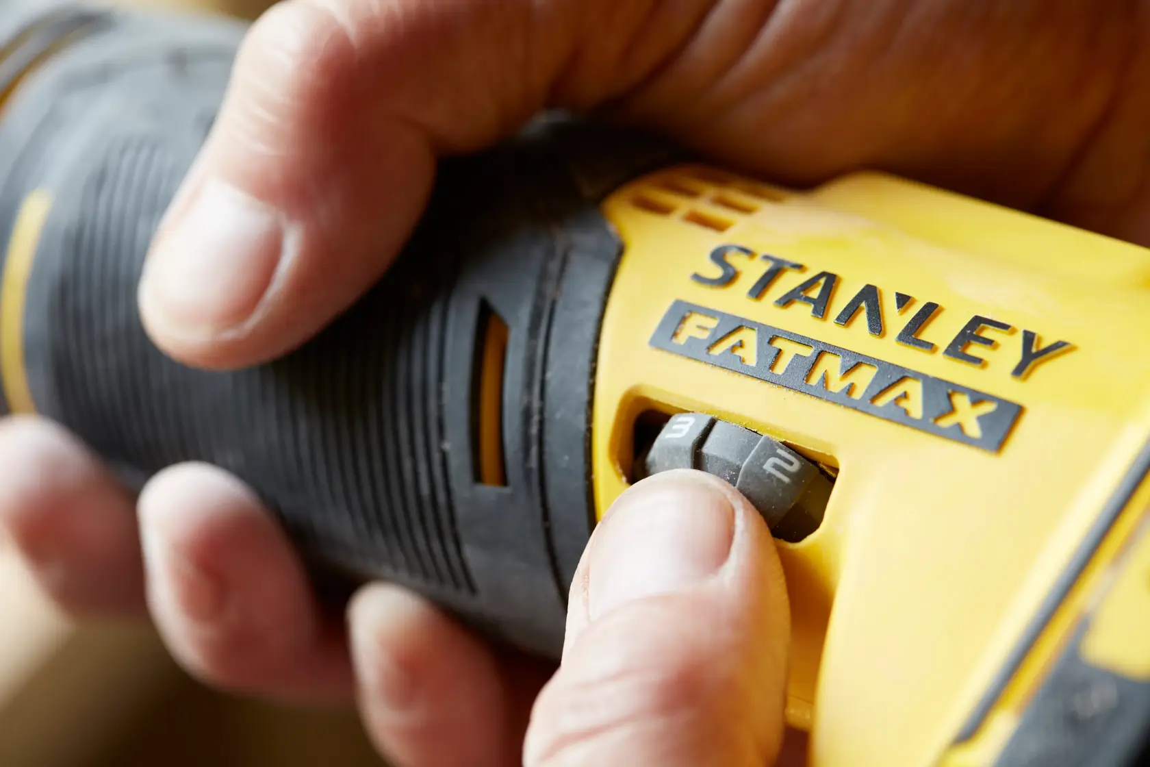 Close-up of STANLEY SFMCE500B FATMAX tool with hand adjusting speed dial, product photography.
