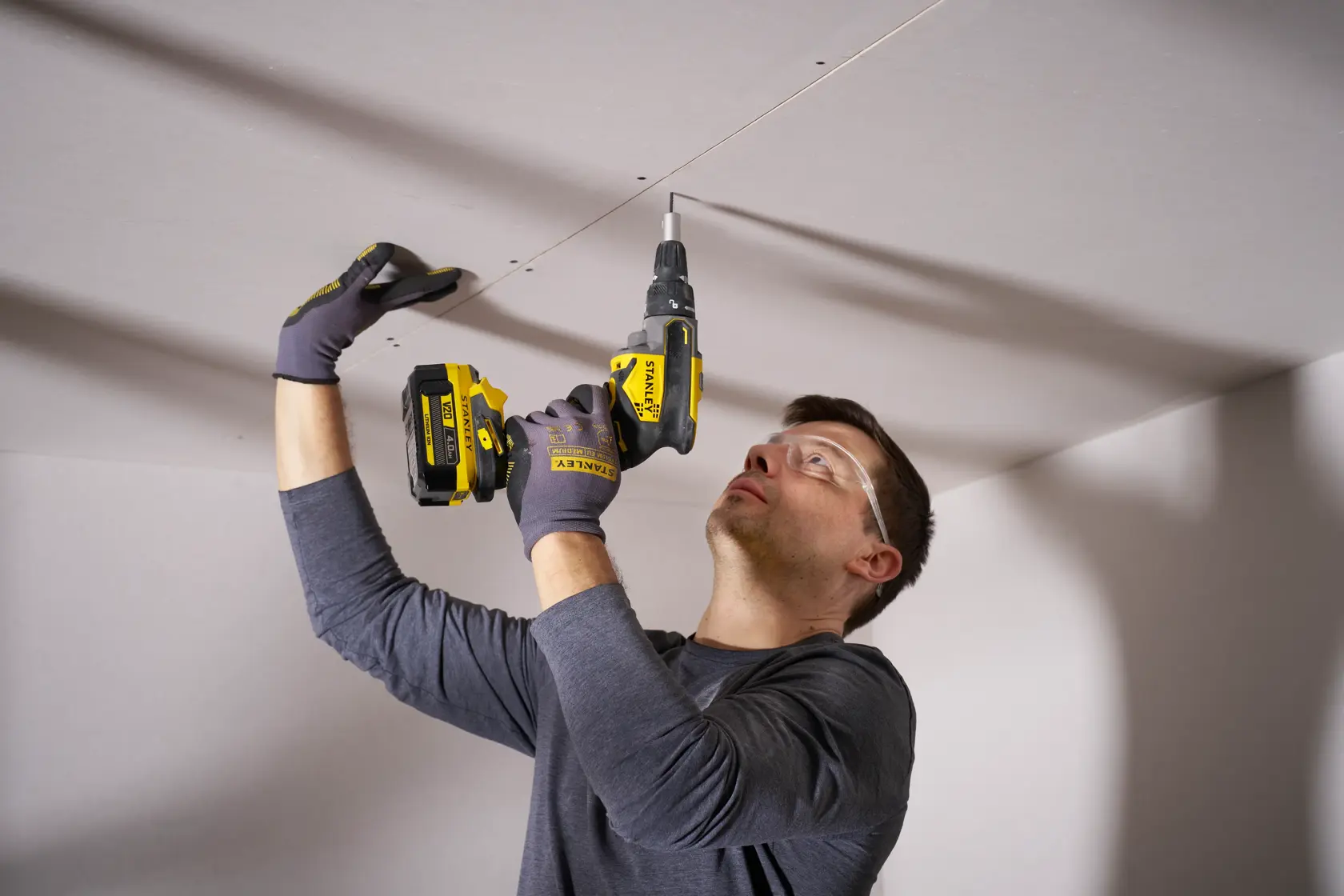 STANLEY SFMCF600B impact driver used to install screws into ceiling drywall, close-up indoor scene.
