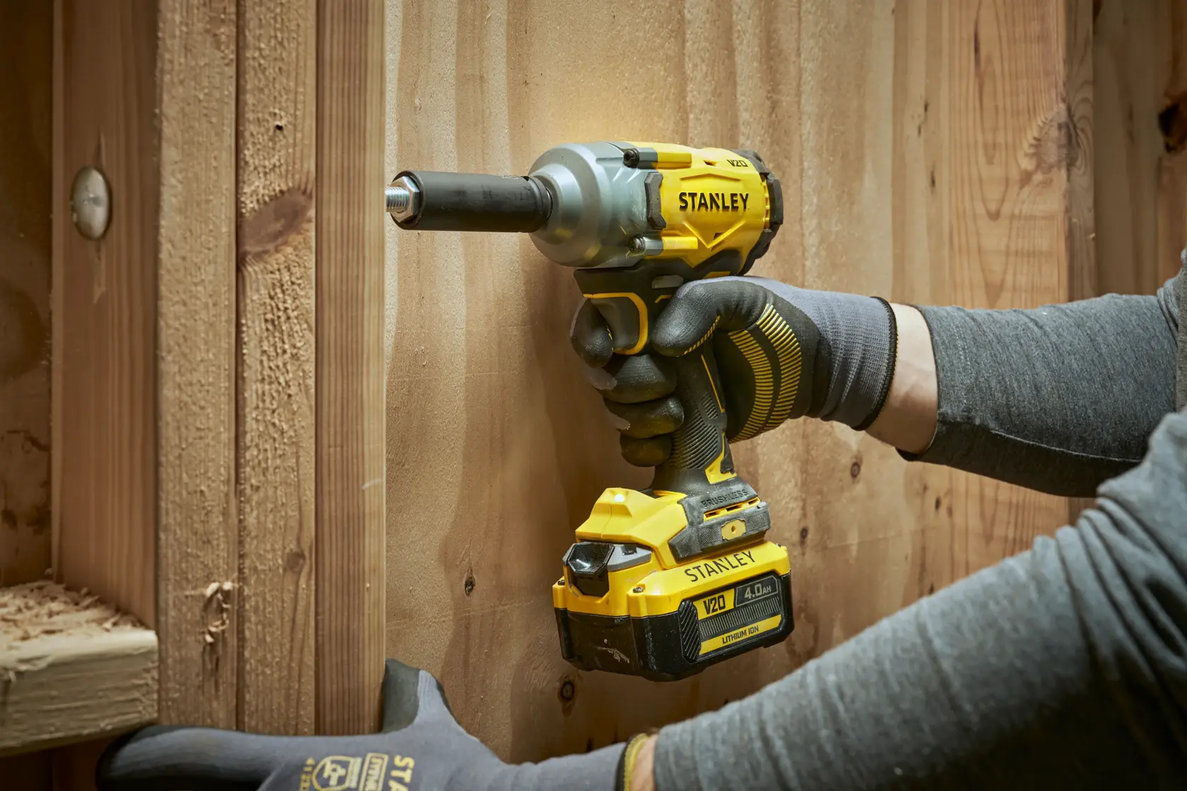 Stanley cordless impact wrench in use on wooden boards, worn by a gloved hand.