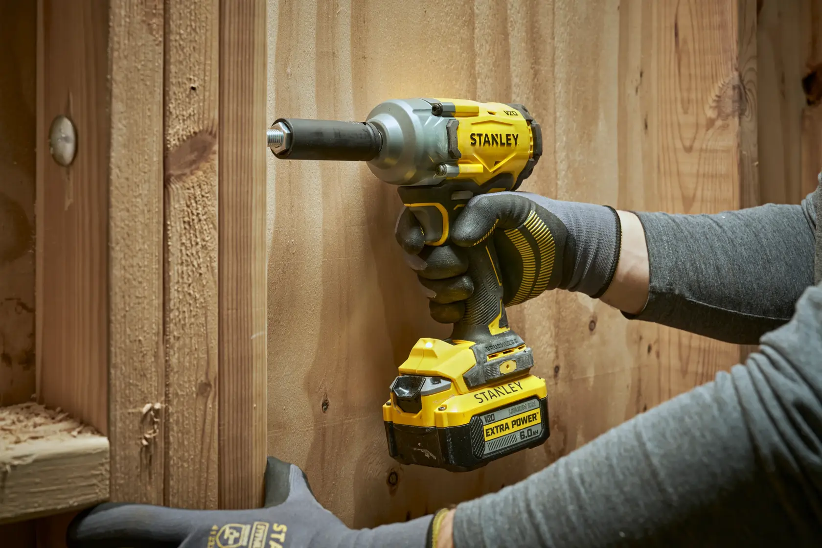 Stanley cordless impact wrench in use on wooden surface, held by gloved hands.