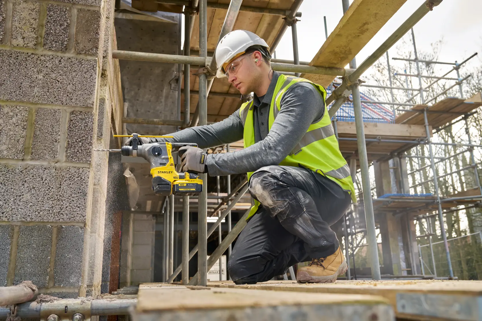 Photo of worker using STANLEY SFMCH910B rotary hammer drill on concrete wall at construction site.