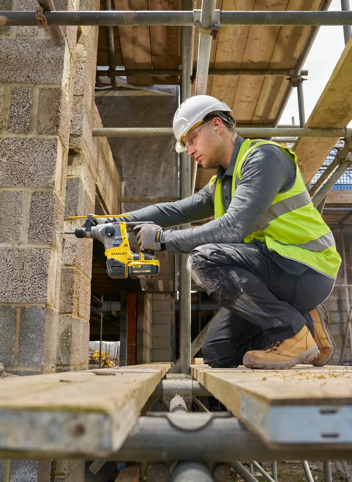 STANLEY SFMCH910B rotary hammer drill in use on a construction site, side view, operator drilling into concrete blocks.