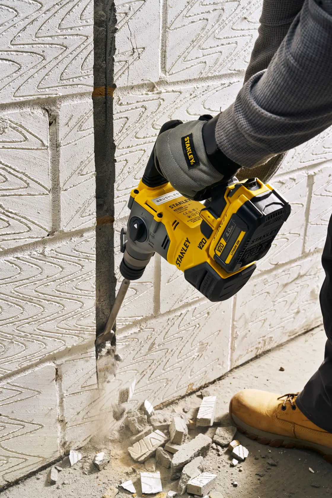 STANLEY SFMCH910B rotary hammer in use chiseling white brick wall, handheld, visible rubble and dust.