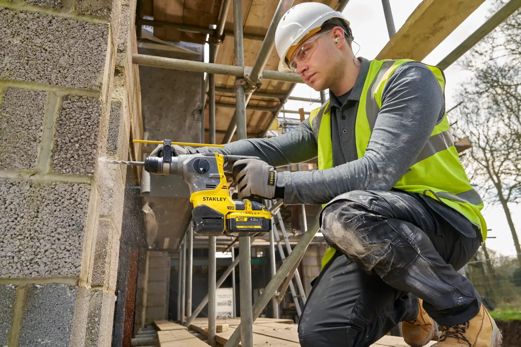 STANLEY SFMCH910M1T rotary hammer drill in use on a construction site drilling into a concrete block wall.