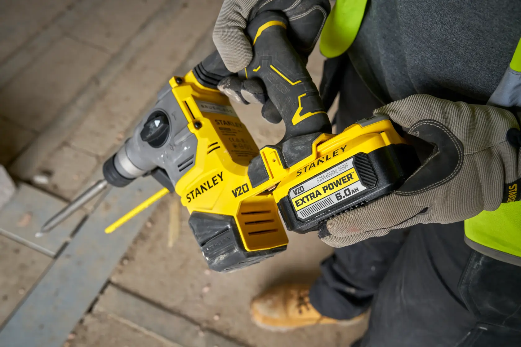 Stanley V20 cordless rotary hammer drill held by a person with gloves, on a construction site.