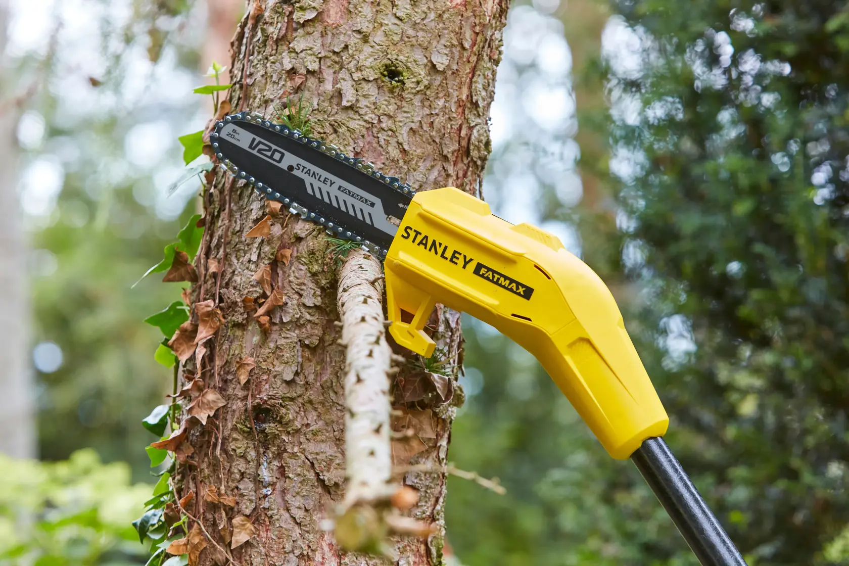 STANLEY SFMCPS620B pole saw cutting tree branch outdoors, yellow body with V20 blade visible.