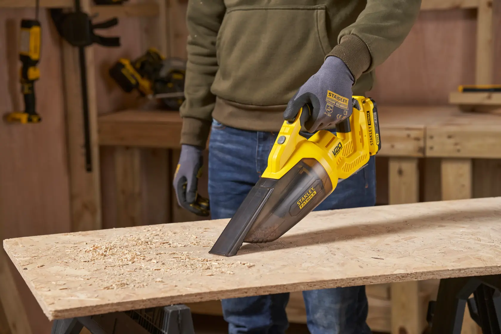 STANLEY SFMCVH001B handheld vacuum in use on wood surface, yellow body, clear dust container.
