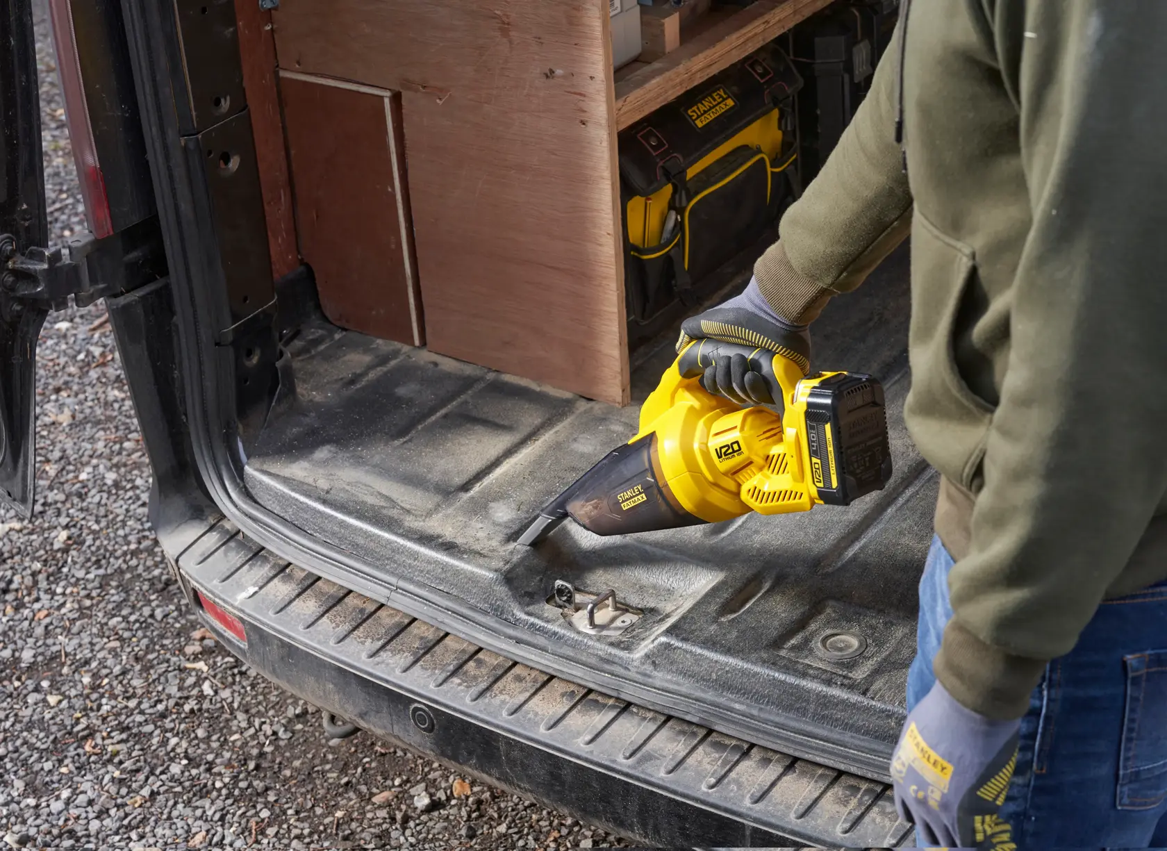 STANLEY SFMCVH001B handheld vacuum cleaner in use cleaning a vehicle trunk, yellow and black color.