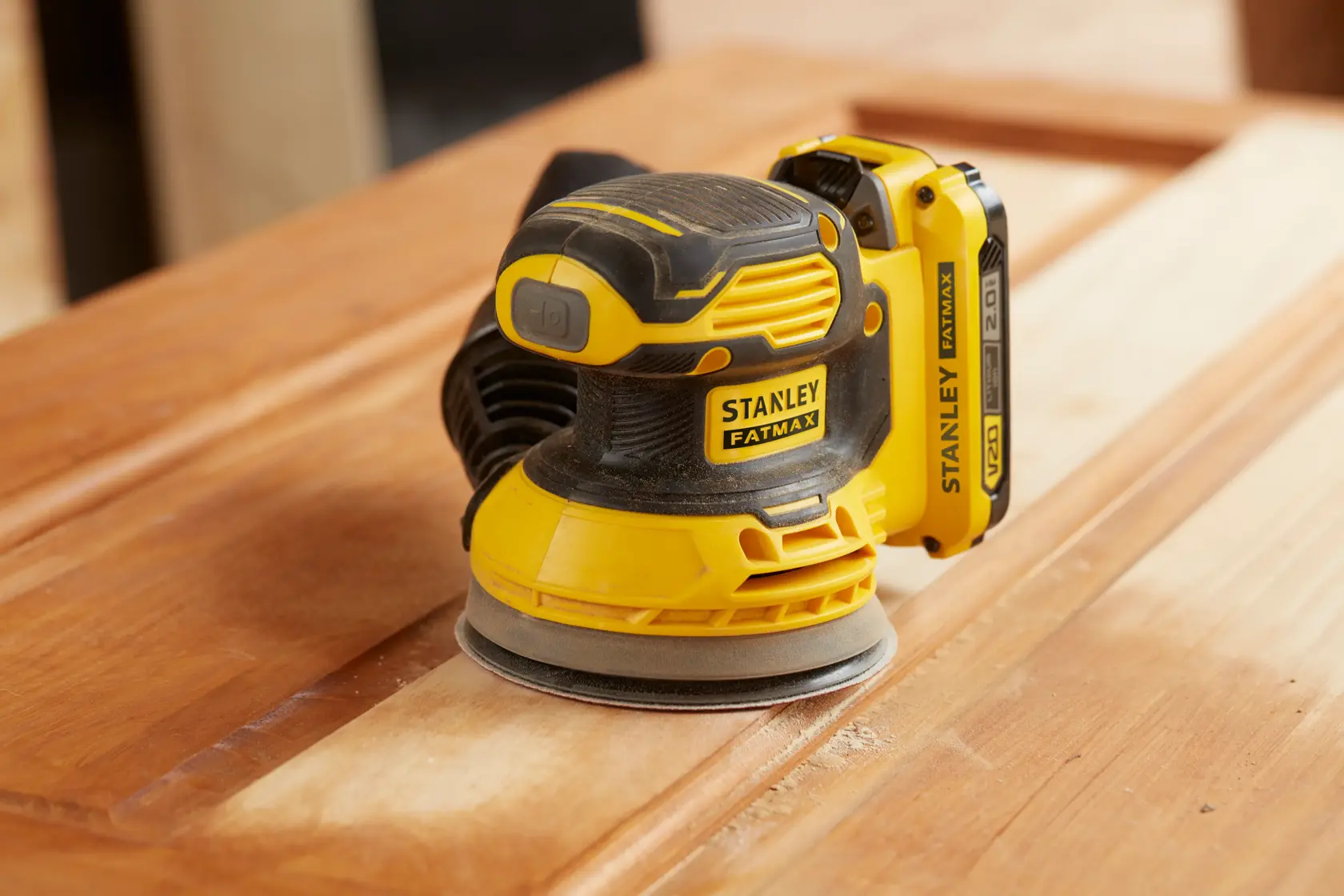 STANLEY SFMCW220D1S cordless orbital sander in yellow and black, sanding a wooden surface.