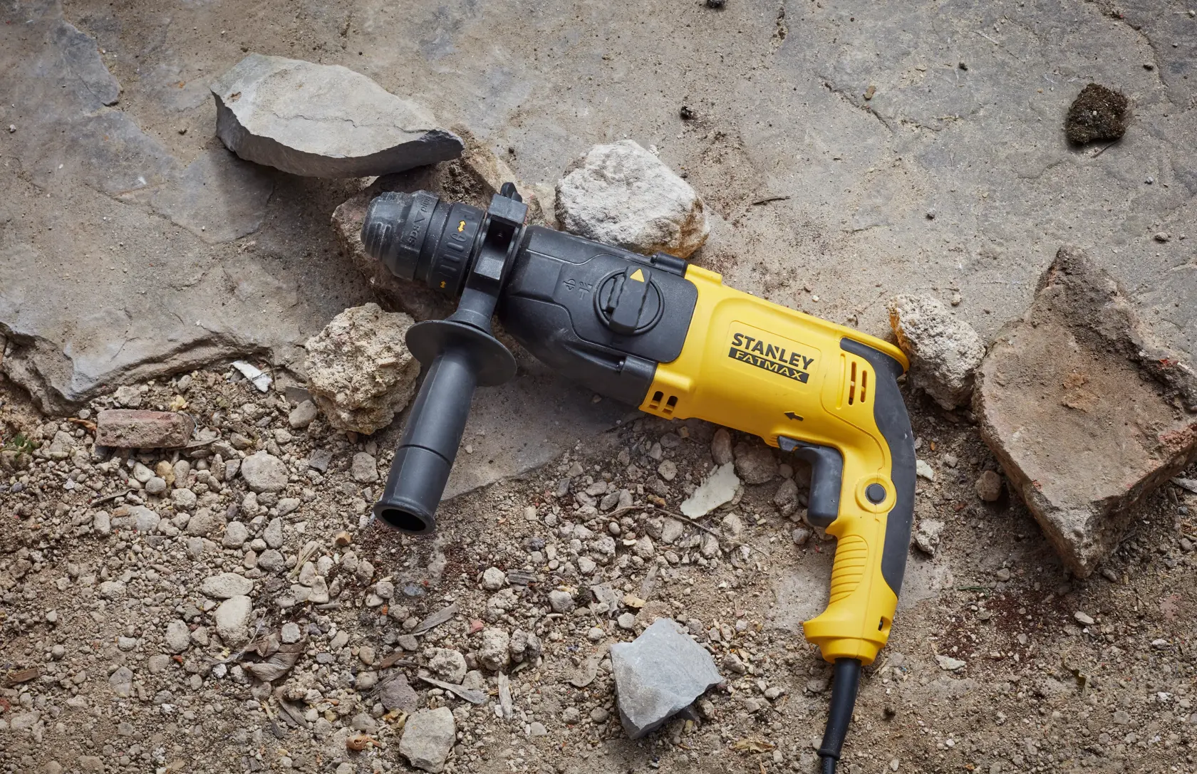 STANLEY SFMEH210K-QS corded hammer drill in yellow and black, placed on rocky ground.