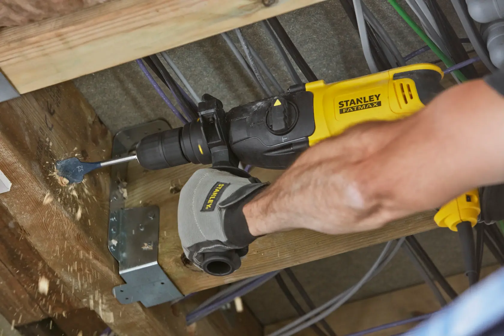 STANLEY SFMEH210K-QS hammer drill in use drilling wood beam, close-up, yellow and black tool, photography.