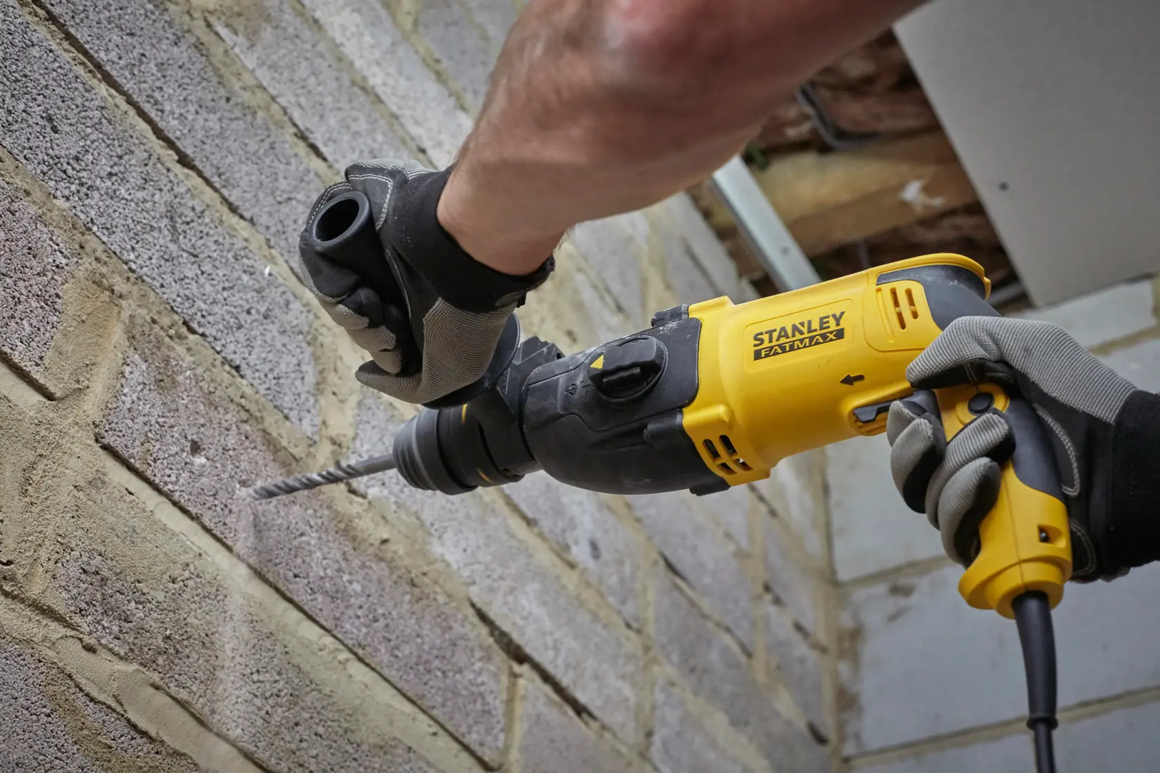 STANLEY SFMEH210K-QS rotary hammer drill in use on a brick wall, close-up of tool and gloved hands.