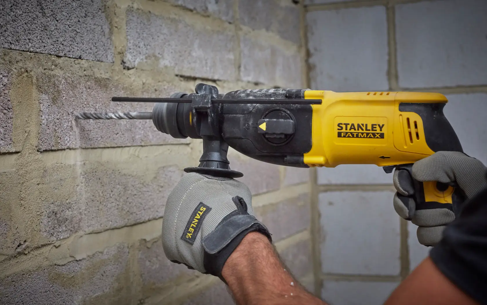 Photo of STANLEY SFMEH210K-QS rotary hammer drill being used on a brick wall, yellow and black design.