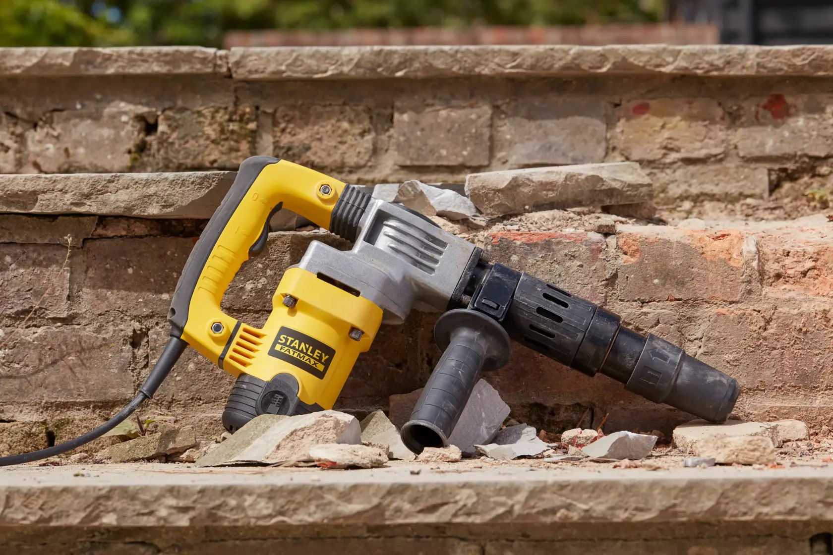 Photo of STANLEY SFMEH220K-QS demolition hammer resting on broken brick steps, yellow and black body, side handle visible.