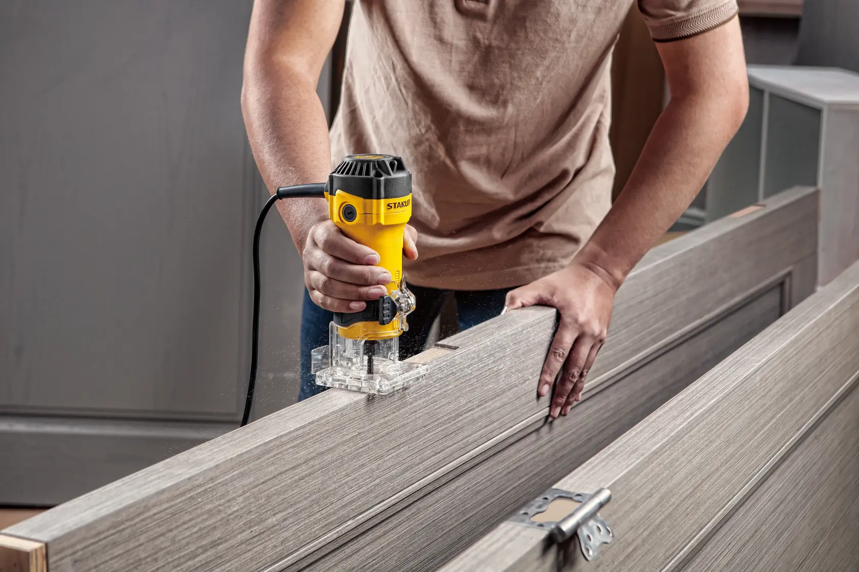 Photo of STANLEY ST55-B2 compact router being used on a wooden door, clear base, user holding tool with one hand.