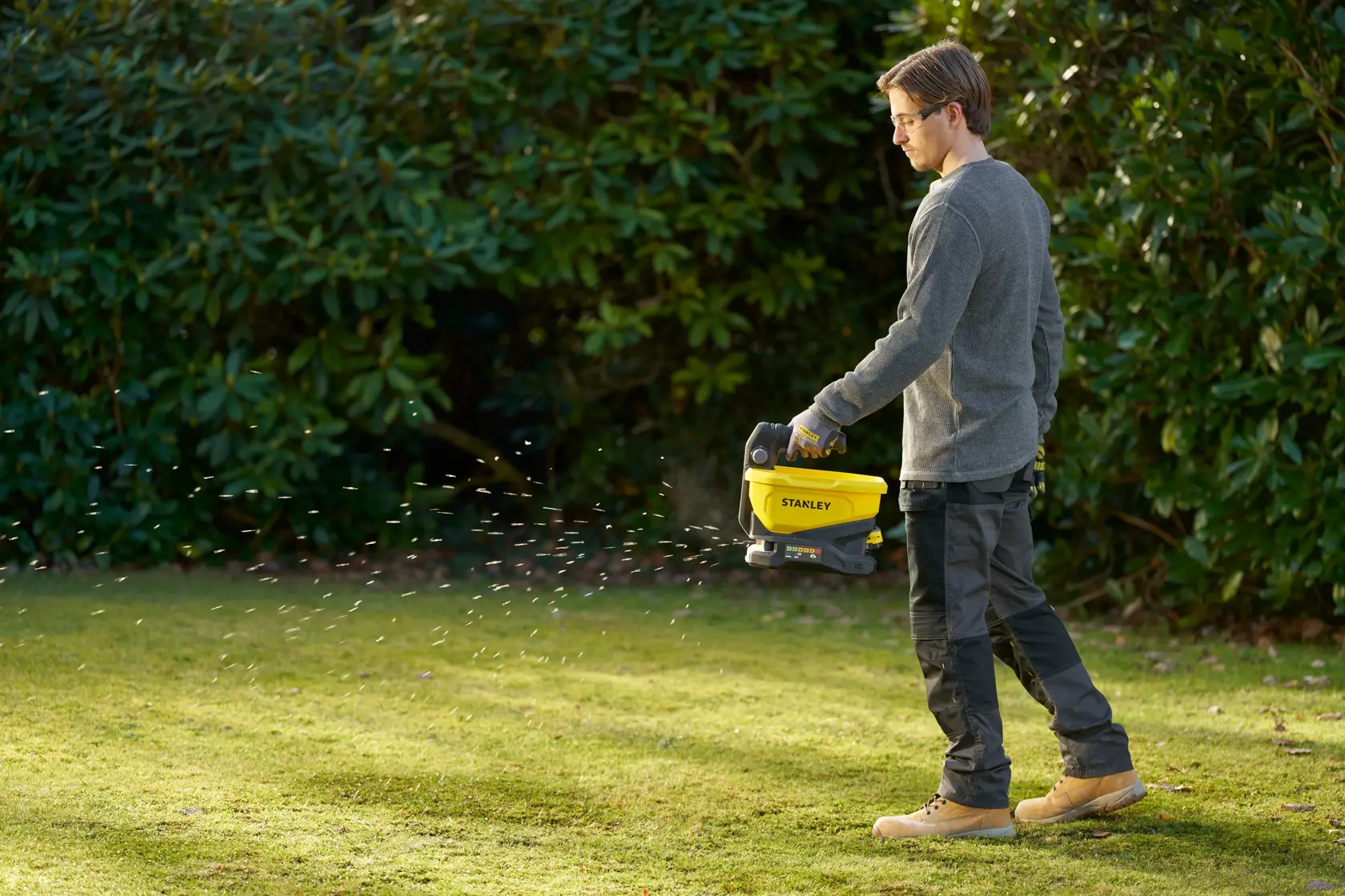 Person using STANLEY STCOE300B spreader on grass in a garden.