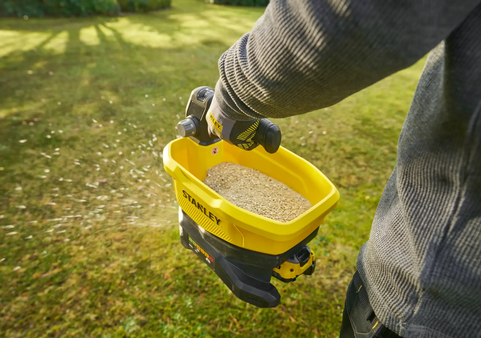 Photo of STANLEY STCOE300B handheld spreader in use, spreading seeds on grass lawn.