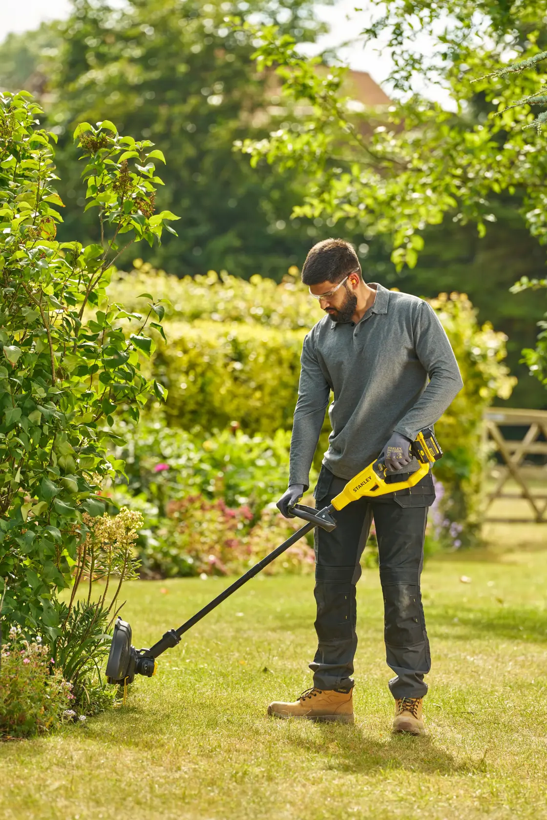 STANLEY STCST933M1 grass trimmer shown outdoors in use by a person, yellow and black design.
