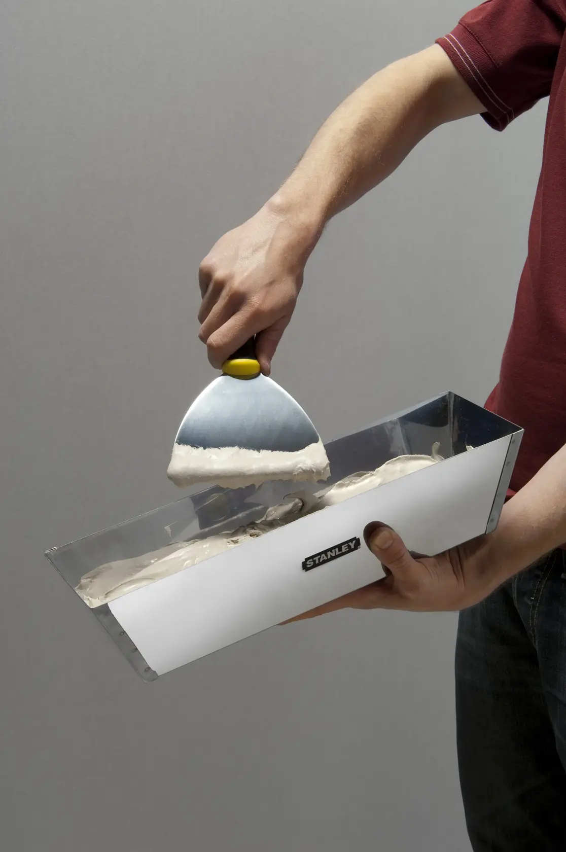 Photo of STANLEY STHT0-05867 taping knife in use, scooping plaster from a metal mud pan.