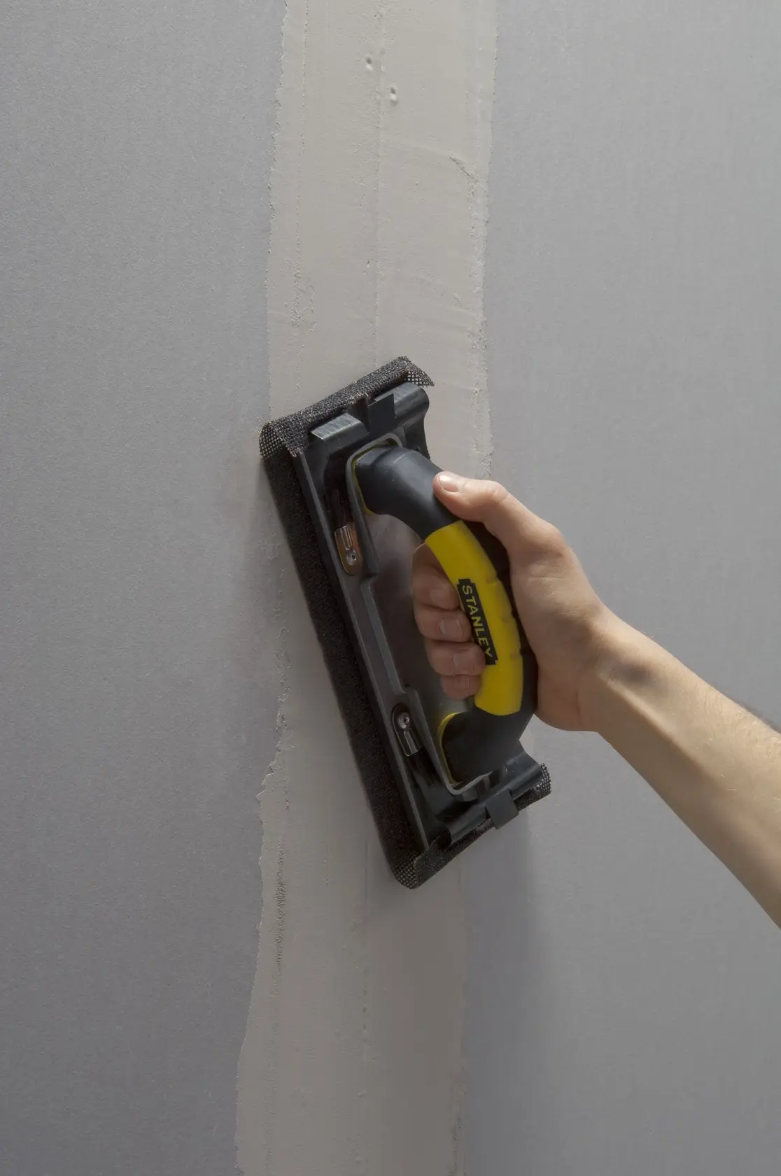 Photo of STANLEY STHT0-05927 hand sander with black and yellow handle sanding wall surface.