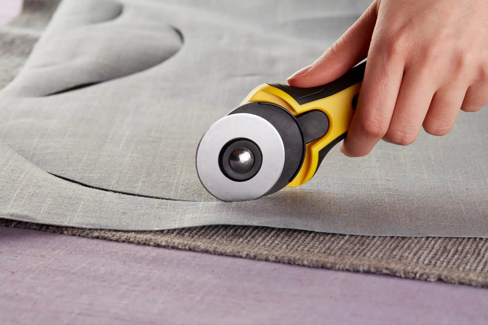 STANLEY STHT0-10194 rotary cutter tool held cutting gray fabric close-up.