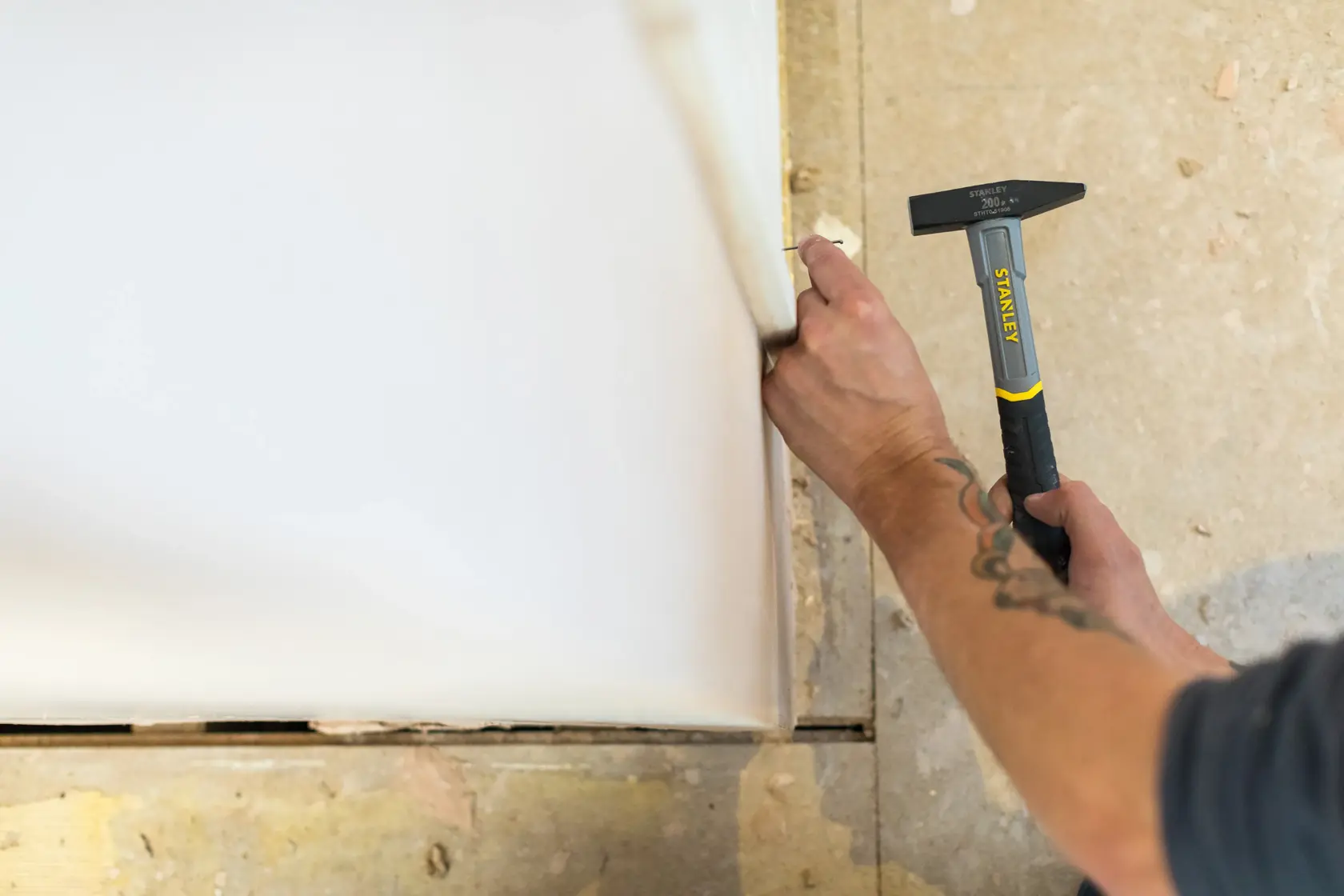 Photo of STANLEY STHT0-51906 hammer in use against drywall, close-up showing tool and user’s hands.