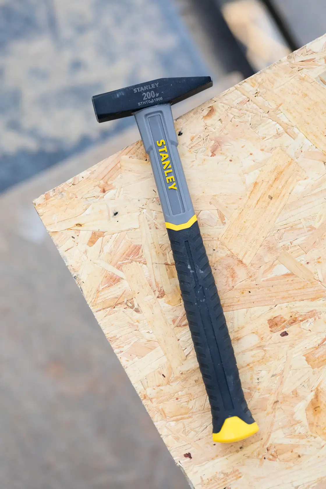 STANLEY STHT0-51906 hammer with black and yellow handle, side view, on plywood board.