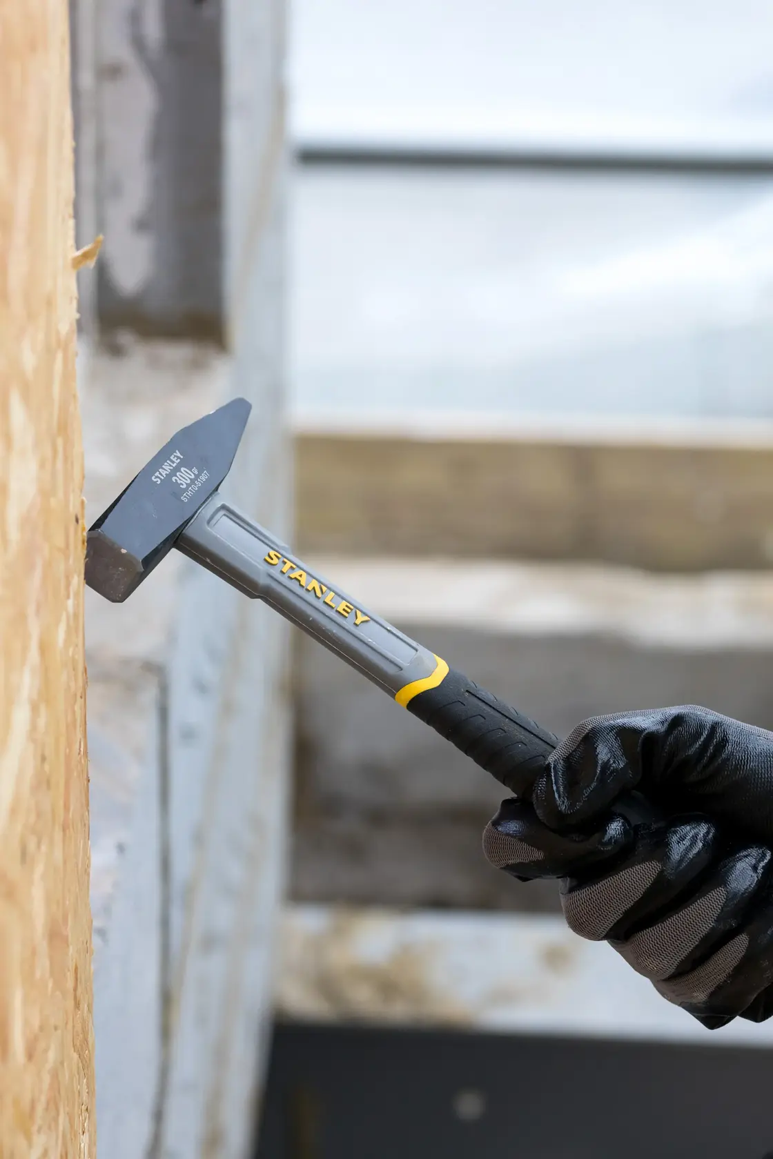Stanley STHT0-51907 hammer with black and yellow handle used against wooden surface, photography close-up.