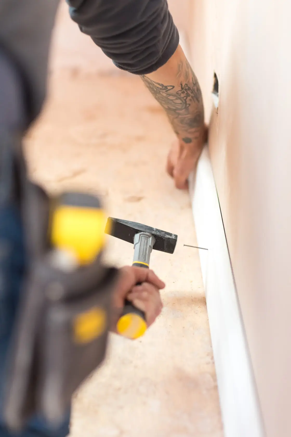 STANLEY STHT0-51908 hammer in use, person nailing baseboard to wall, close-up side photography.